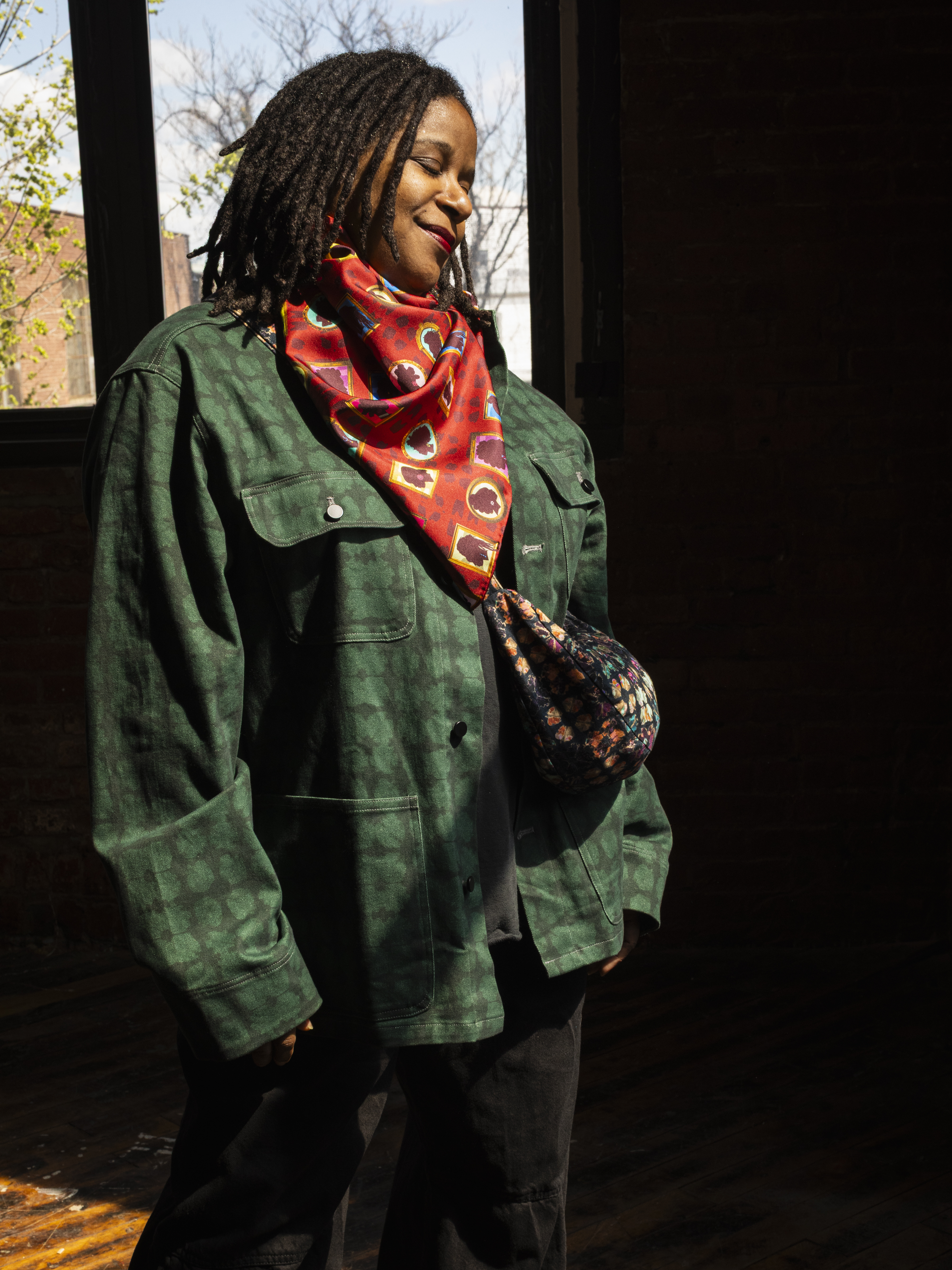 photo of black woman with an afro wearing a t-shirt that reads: Minding my own Black Business. Woman is seated next to three large and colorful zipper pouches.